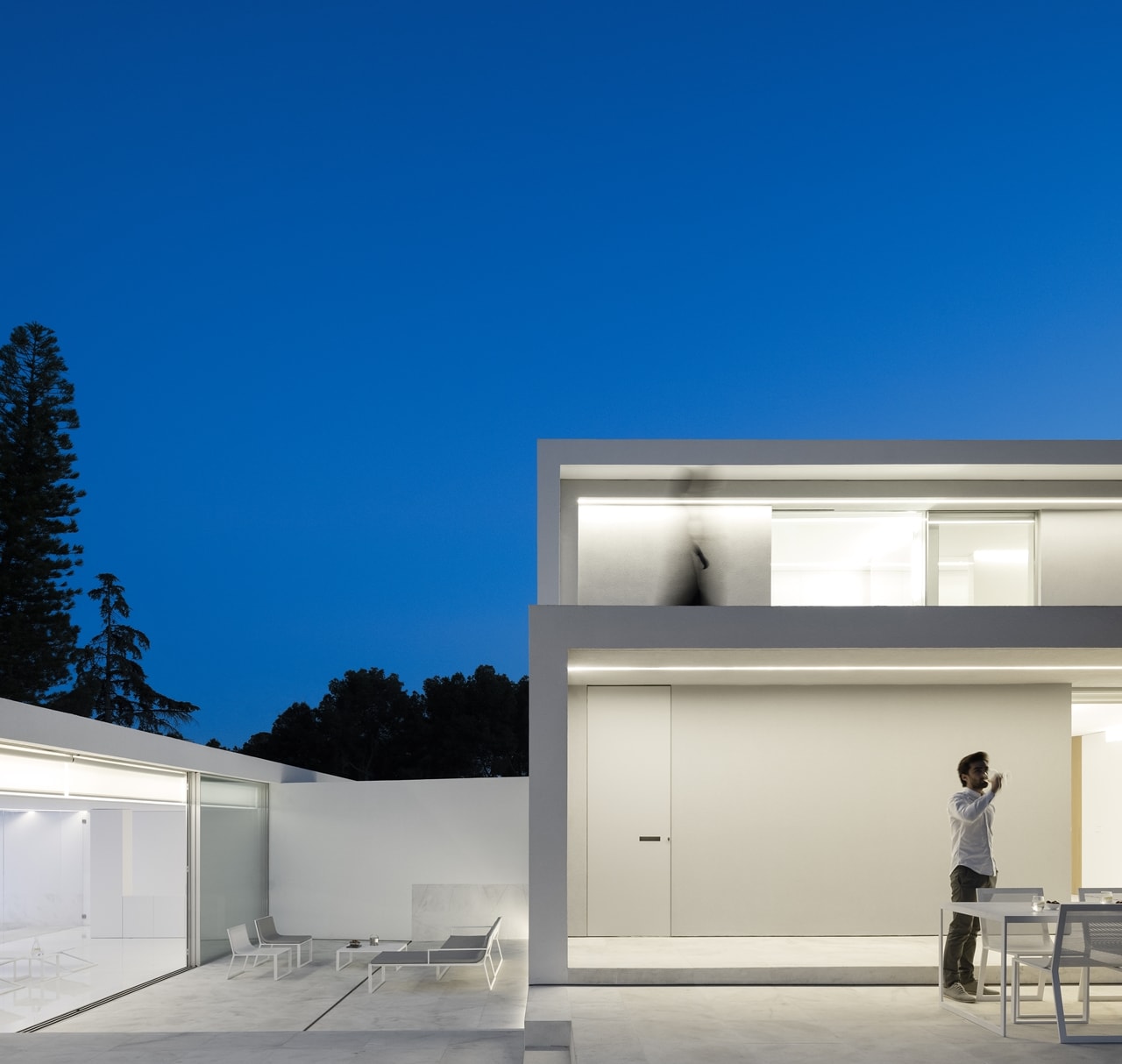 White facade of minimalist house designed by Fran Silvestre Architects lit up at night